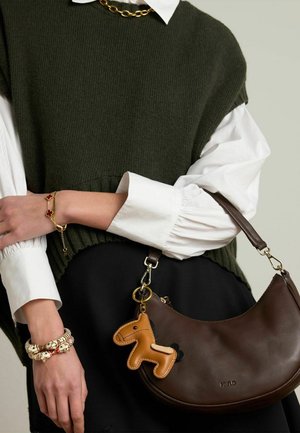 Brown leather handbag with a curved shape and a horse-shaped charm. Worn with a dark skirt and a green knitted top over a white shirt.