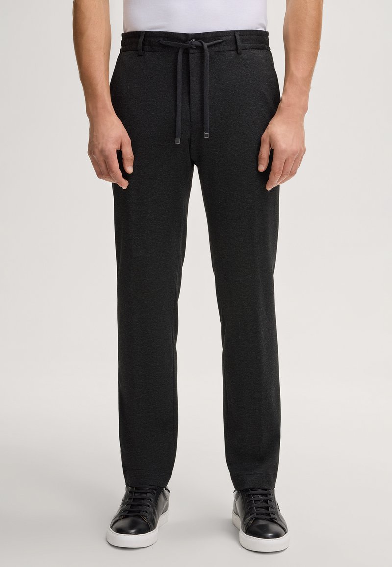 Pantaloni jogger neri da uomo in morbido tessuto, con vita regolabile tramite cordoncino, vestibilità slim e finitura leggermente testurizzata. Abbinati a sneakers nere.