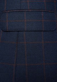 Granatowy materiał z delikatnym wzorem kratki w odcieniach pomarańczowego i brązowego, z kieszonką w lewym górnym rogu, o teksturowanym splocie.