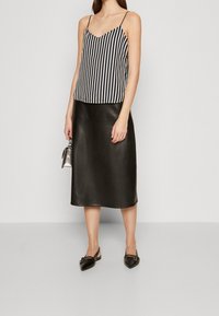 Schwarz-weiß gestreiftes Satin-Cami mit dünnen Trägern, kombiniert mit einem schwarzen Leder-Midiskirt. Abgerundet mit spitzen schwarzen Schuhen.