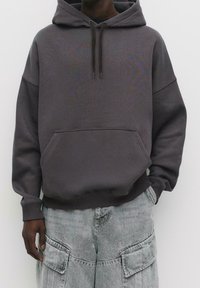 Sweat à capuche gris foncé avec une poche kangourou, doté d'une coupe décontractée, d'une fermeture à cordon de serrage et de poignets et ourlet côtelés.