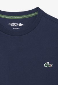 Camiseta de corte regular Lacoste Sport en azul marino con logo de cocodrilo verde en el pecho y un ribete de cuello verde cosido.