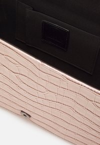 Vaaleanpunainen teksturoitu nahkapenkkilaukku, jossa on krokotiilikuosi ja musta kangaspussi, jossa on ommeltu etiketti.