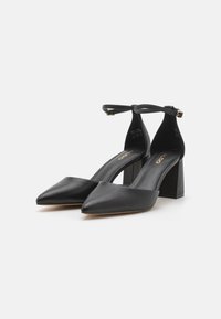 Black high-heeled shoes with a pointed toe and ankle strap, featuring a textured block heel and smooth leather upper.