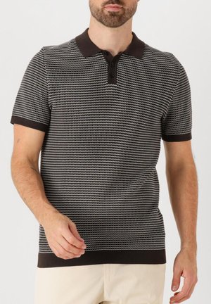 Uomo che indossa una polo a maniche corte con motivo bianco e nero, colletto e polsini neri, abbinata a pantaloni beige chiaro.