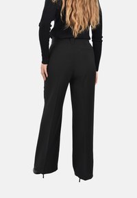 Pantaloni neri a gamba larga con una texture liscia, dotati di una tasca posteriore e di una leggera apertura all'orlo per un tocco di design in più.