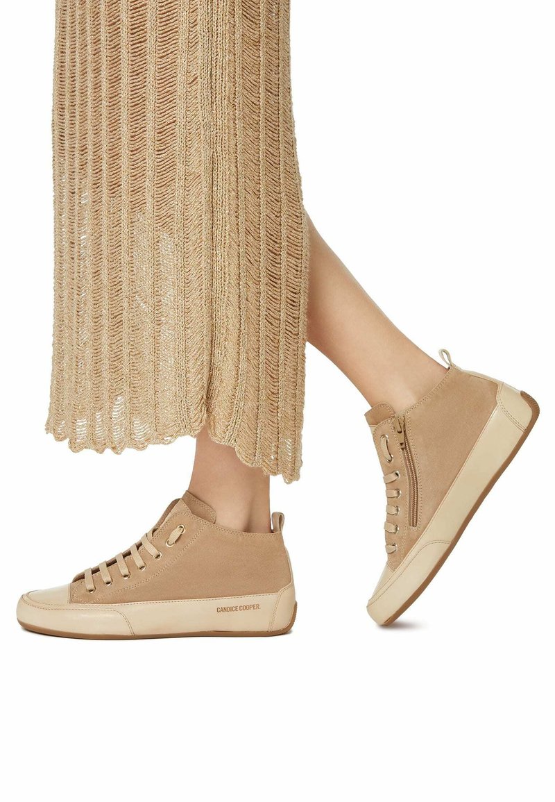 Sneakers alte in suede color cammello con suola in gomma crema, dotate di lacci, cerniera laterale e logo sul tallone. La texture è morbida e opaca.