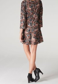 Short-sleeved dress in dark floral pattern with maroon, blue, and white tones. Hemline flares at the bottom, paired with black ankle boots.