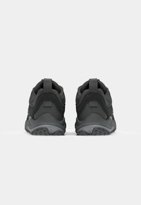 Black athletic shoes viewed from the back, featuring textured soles and pull tabs, against a plain white background.
