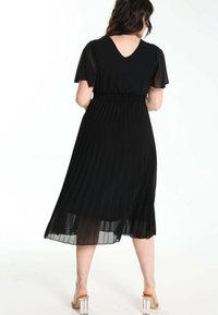 Robe noire plissée à manches courtes et décolleté en V ; comporte une taille élastique et un tissu transparent ; longueur mi-mollet avec une silhouette fluide.