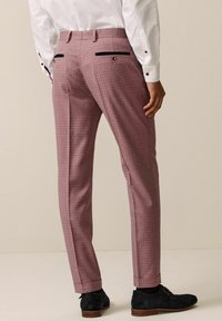 Maßgeschneiderte Hosen in einem hellrosa Karomuster. Mit Seitentaschen und navyfarbenen Akzenten. Kombiniert mit einem weißen Hemd und dunklen Schuhen.