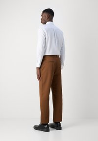 Brown trousers with a straight cut, crafted from cotton. Paired with a white long-sleeve shirt and black leather shoes.