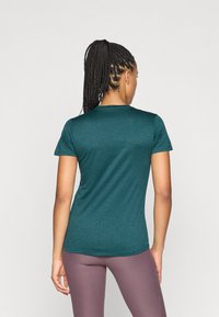 Teal tett skjorte med korte ermer, rund hals og myk tekstur. Sammen med lyse lilla tights, sett bakfra.