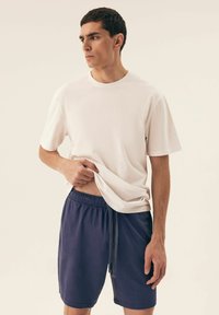 Biała bawełniana koszulka z krótkim rękawem, noszona z granatowymi szortami na sznurki. Prosty design, luźny krój, subtelne tekstury i stonowane kolory.