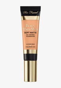 Too Faced Born This Way Soft Matte Oil Control Foundation in einer Quetschtube. Weicher Pfirsichfarbton, schwarzer Deckel und goldene Akzente. 24-Stunden-Trageformel.