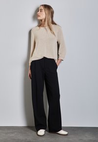 Top a maglia beige con scollo rotondo e maniche a tre quarti; abbinato a pantaloni neri a vita alta con gamba larga e sneakers bianche.