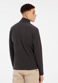 Donkergrijze, gestructureerde pullover met een hoge kraag en lange mouwen. Heeft een ruitpatroon en een rechte zoom, gecombineerd met lichtgekleurde broeken.