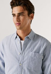 Camicia a bottoni a righe blu e bianche realizzata in tessuto leggero, con taschino sul petto e colletto classico. Motivo testurizzato visibile.