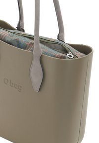 Taupe O Bag Tote mit grauen Griffen und einem Reißverschluss-Fabric-Einsatz, der ein mehrfarbiges Karomuster im Hauptfach der Tasche aufweist.