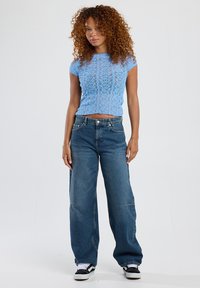 Light blue, short-sleeve knitted top paired with loose-fitting, mid-blue jeans. Shoes are black and white sneakers.