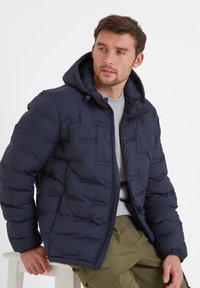 Navy puffer jacket with a hood, featuring a quilted design, zip closure, and elastic cuffs. Worn over a gray shirt.