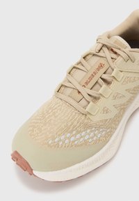 Beige løbesko med strikket mesh-overdel, tekstureret overflade, ekstra polstring, gummisål og kontrasterende tan-detaljer.