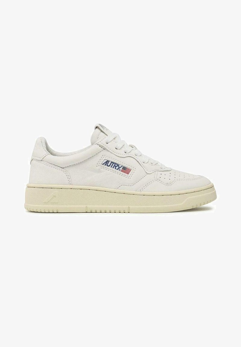 Sneaker in pelle bianca con superficie testurizzata, caratterizzata da un profilo basso, punta rotonda, dettagli perforati e una suola beige a contrasto.