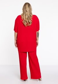 Rode geribbelde twee-delige outfit bestaande uit een losvallend top met korte mouwen en een wijde broek, beiden in een gestructureerde stof.