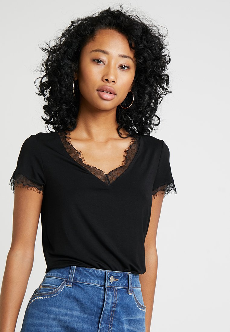 T-shirt noir à manches courtes avec un col en V et des garnitures en dentelle autour du col et des manches, associé à un bas en denim bleu.