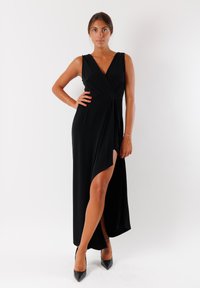 Abito nero avvolgente con scollatura a V profonda, design senza maniche e spacco alto fino alla coscia. Realizzato in tessuto liscio, abbinato a décolleté neri a punta.
