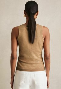 Złoty metaliczny top bez rękawów o dopasowanym kroju i prążkowanym dekolcie, połączony z białymi spodniami z wysokim stanem. Gładka faktura z lekkim połyskiem.