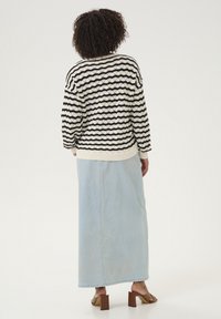 Pull en tricot noir et crème à rayures avec un motif texturé, associé à une jupe maxi en denim bleu clair et des sandales à talons carrés marron.