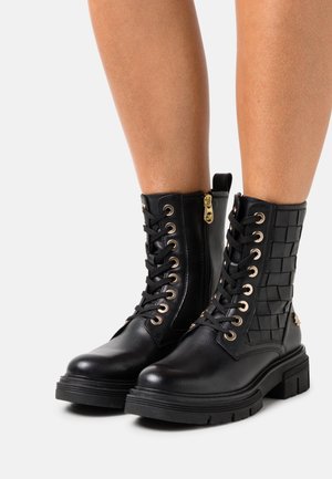 Zwarte enkellaarzen met een gestructureerd geweven zijpaneel, ronde gouden oogjes, veters aan de voorkant en een ritssluiting aan de zijkant met gouden details.