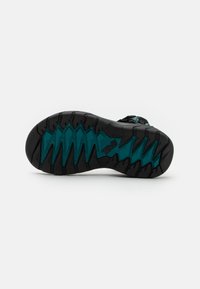 Semelle de chaussure de randonnée noire avec un motif de zigzag turquoise, dotée d'une caoutchouc texturé pour l'adhérence et d'un bord renforcé pour la durabilité.