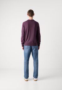 Felpa viola con maniche lunghe, polsini e orlo a costine. Abbinata a jeans azzurri a gamba dritta e sneaker bianche.