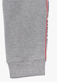 Grijze joggingsbroek gemaakt van een katoenmix. Heeft ribgebreide boorden en zijkanten in rood en blauw met het "GUESS" logo. Zachte textuur.