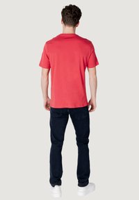 T-shirt rossa a maniche corte con collo tondo, realizzata in cotone, abbinata a jeans blu scuro e sneakers bianche, vista da dietro.