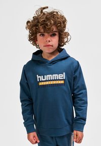 Marineblauer Hoodie aus weichem Stoff mit einem großen „hummel SPORTSWEAR“-Logo in Weiß und Orange auf der Brust sowie einer aufgesetzten Tasche vorne.