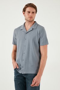 Camisa de manga corta de botón en tejido texturizado gris claro con cuello muesca y seis botones frontales, combinada con jeans de mezclilla oscuros.