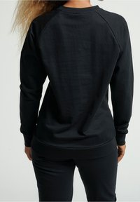 Black sweatshirt with long sleeves and ribbed hem, featuring a smooth texture and a crew neck design, shown from the back.