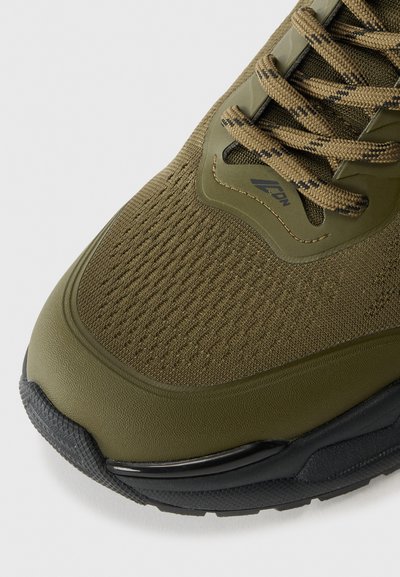 Olive green athletic shoe featuring a textured mesh upper, reinforced toe, and black rubber outsole. Round laces with a patterned design.