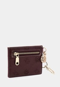 Porte-cartes en cuir bordeaux avec motif embossé, fermeture éclair dorée et breloque en métal attachée. Texture lisse avec des coutures contrastées.