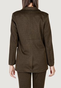 Blazer marrón en espiga con un corte entallado, una abertura trasera y solapas de muesca. Textura suave, adecuado para ropa formal o de negocios.