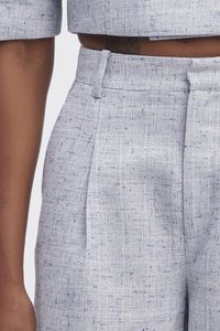 Pantalon ajusté bleu clair en tissu texturé avec des éclats subtils. Présente un devant plat et des plis latéraux pour un ajustement structuré.