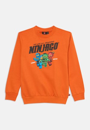 Narančasta dukserica s Lego Ninjago likovima u plavoj, zelenoj i crvenoj boji, sa natpisom "Svi smo zmajevi, Ninjago jači zajedno" na prednjoj strani.