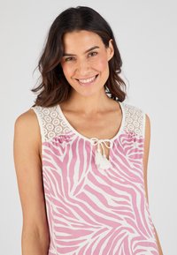Top senza maniche di colore rosa con strisce bianche a zebra, caratterizzato da un corpetto all'uncinetto, scollatura a chiave e nappine decorative al dettaglio del nodo.