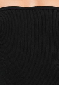 Μαύρο ριχτό τοπ χωρίς τιράντες φτιαγμένο από ελαστικό ύφασμα. Η υφή διαθέτει κατακόρυφες ραβδώσεις, προσφέροντας μια εφαρμοστή σιλουέτα χωρίς μεταλλικά εξαρτήματα.