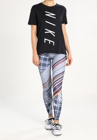 Czarny t-shirt z krótkim rękawem z białym logo "NIKE", zestawiony z legginsami w wzory z ukośnymi paskami w kolorach niebieskim, czerwonym i szarym. Białe sneakersy.