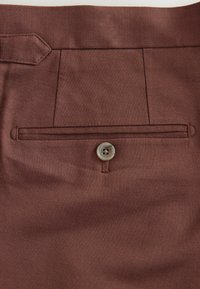 Brown fabric featuring a flat front design with a single back pocket, accented by a small button. Soft texture with a woven pattern.