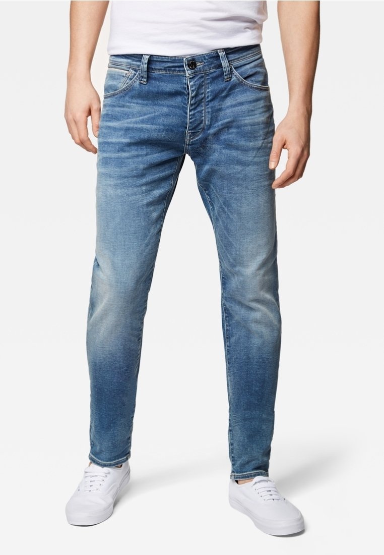 Jeans de mezclilla en azul claro con corte slim, áreas deslavadas, diseño de cinco bolsillos y cierre de botón, combinados con zapatillas blancas.